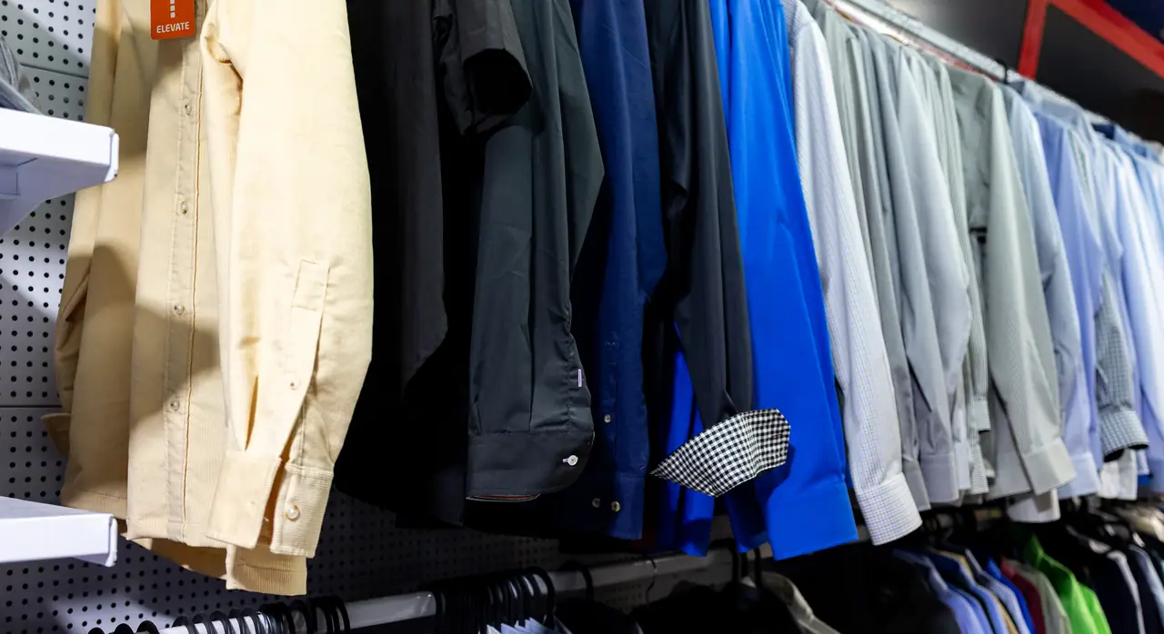 Percheros con camisas de uniforme en blanco, azul y gris en la tienda de Dyreco